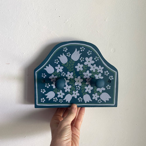 Decorative wall hook with floral design held by a hand against a white background
